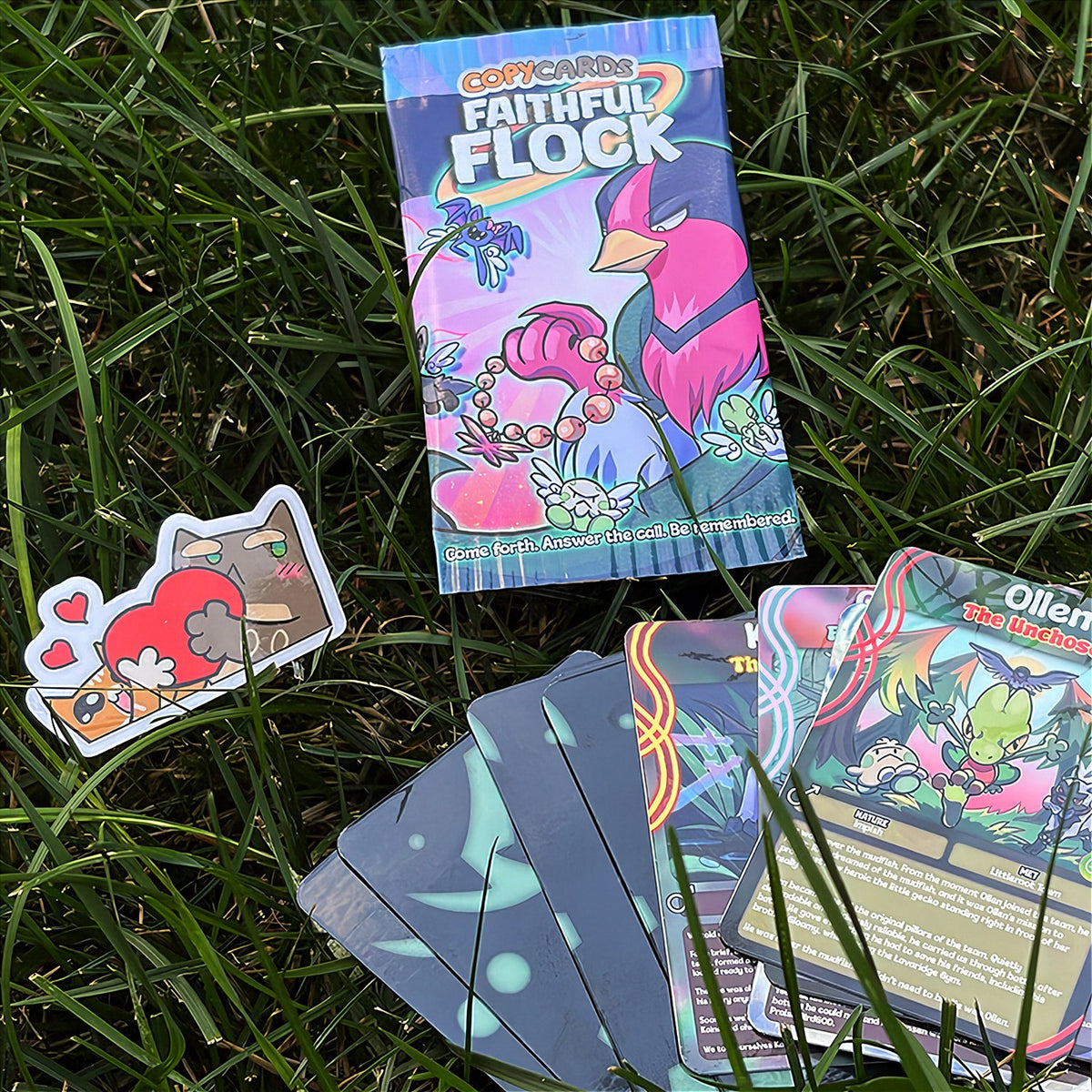 A hand holds a cartoon sticker next to a printed card pack titled "CopyCards Faithful Flock" on grass outdoors.
