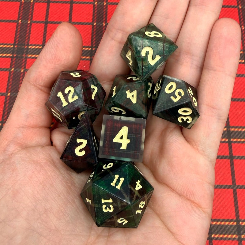 Hand holding a set of green polyhedral dice with yellow numbers on a red plaid background