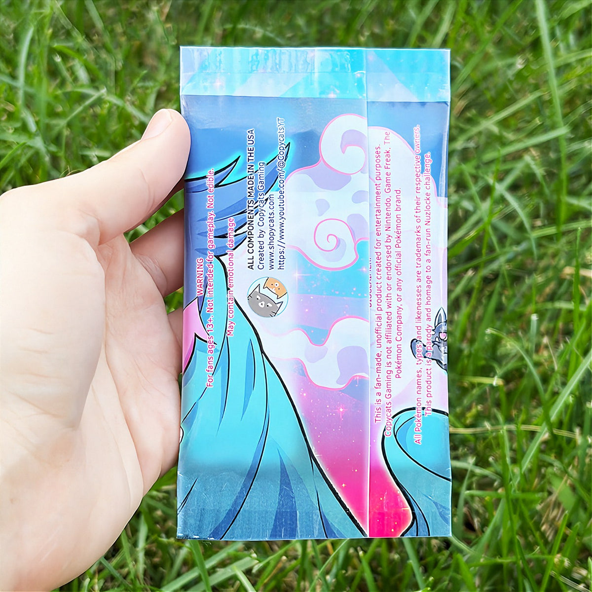 A hand holds a cartoon sticker next to a printed card pack titled "CopyCards Faithful Flock" on grass outdoors.