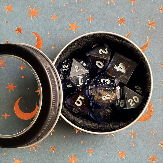 Set of polyhedral dice in a tin with star and moon pattern
