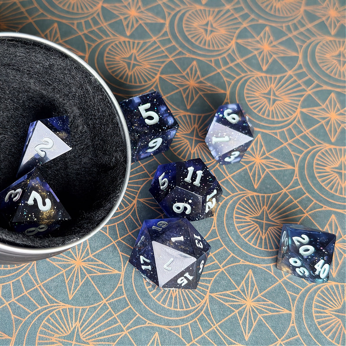 Set of polyhedral dice in a tin with star and moon pattern