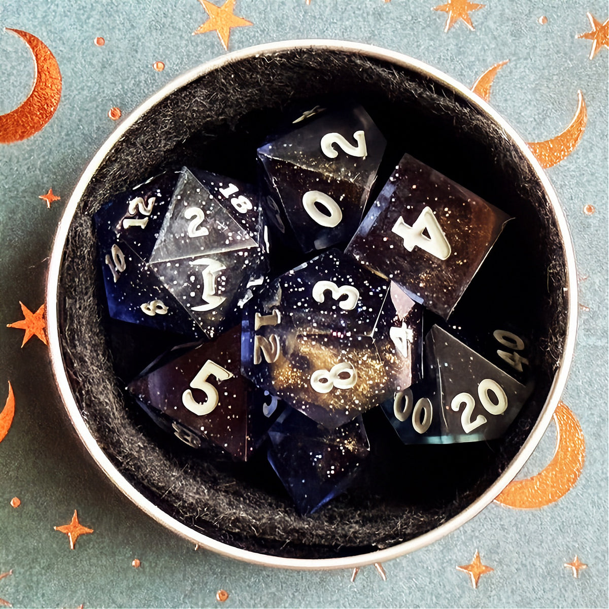 Set of polyhedral dice in a tin with star and moon pattern