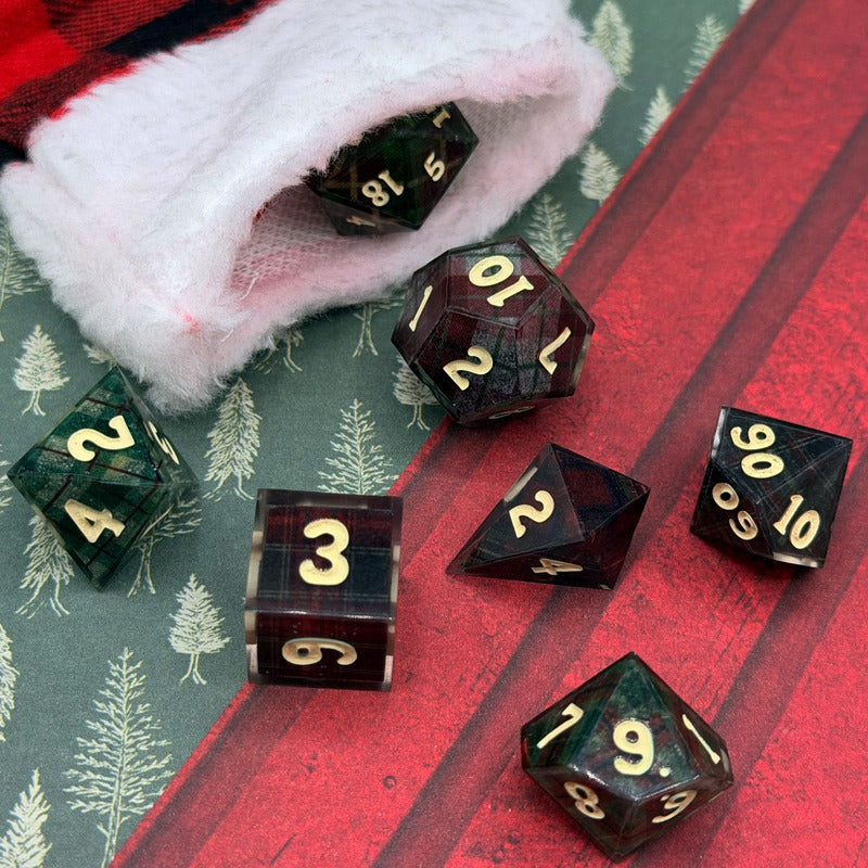 Set of polyhedral dice with gold numbers on a red and green checkered background.