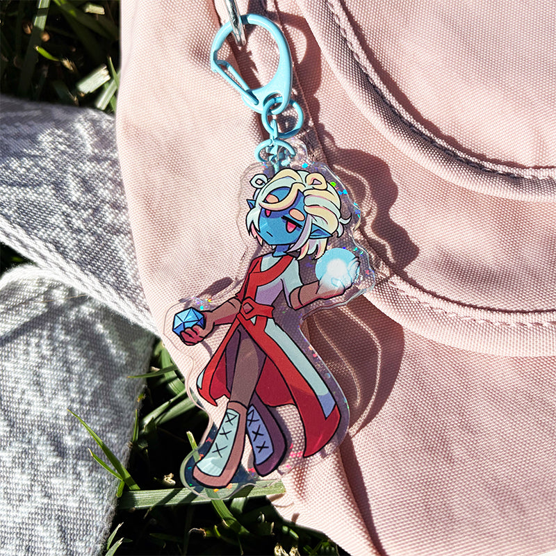 Character keychain with colorful design held against a pink fabric background