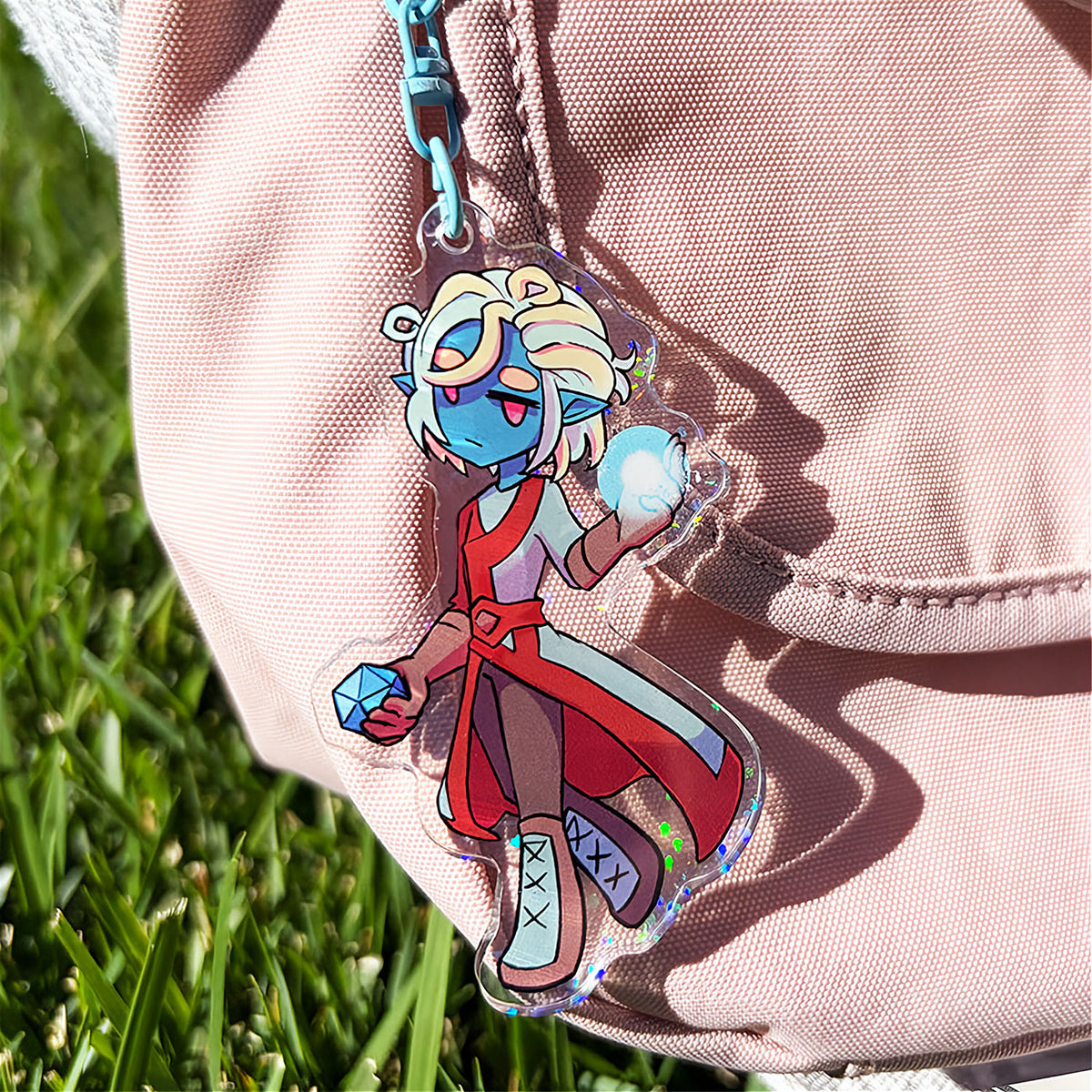Colorful character keychain attached to a beige jacket with grass in the background