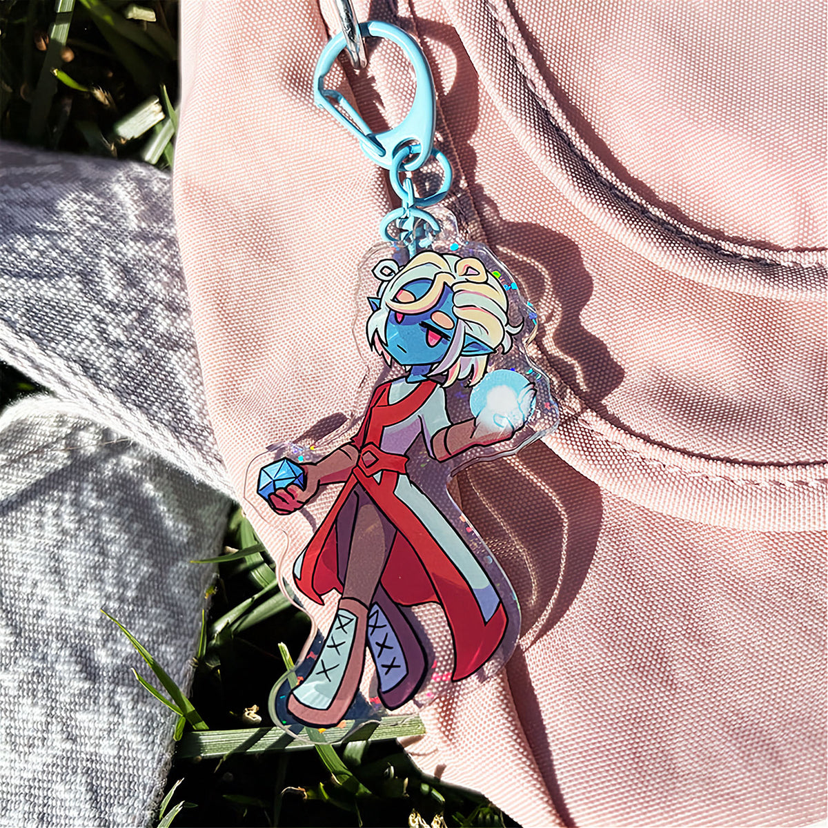 Colorful character keychain attached to a beige jacket with grass in the background
